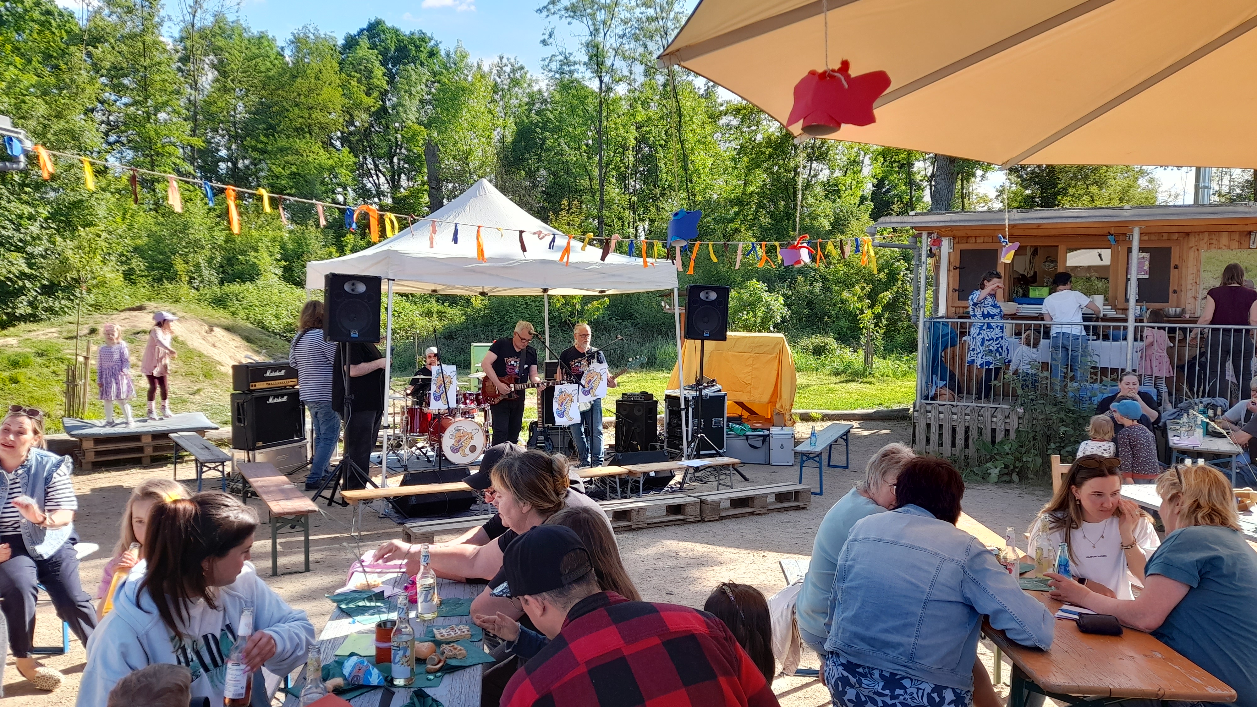 Besucher an Tischen vor kleiner Bühne mit Musikern