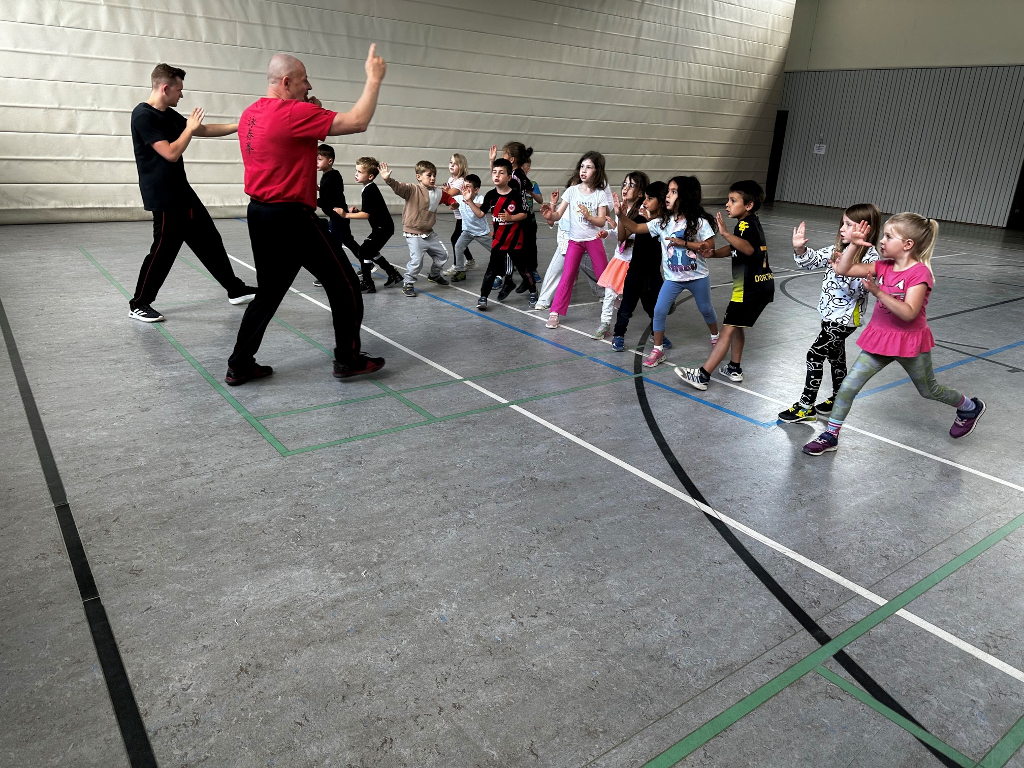 Zwei Trainer und Kinder in Aktion im Ausfallschritt mit erhobenen Händen