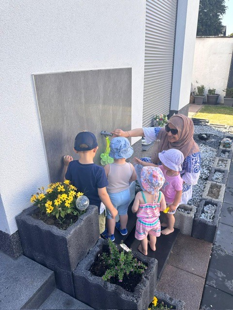 Tagesmutter und Kinder spielen draußen mit Wasser