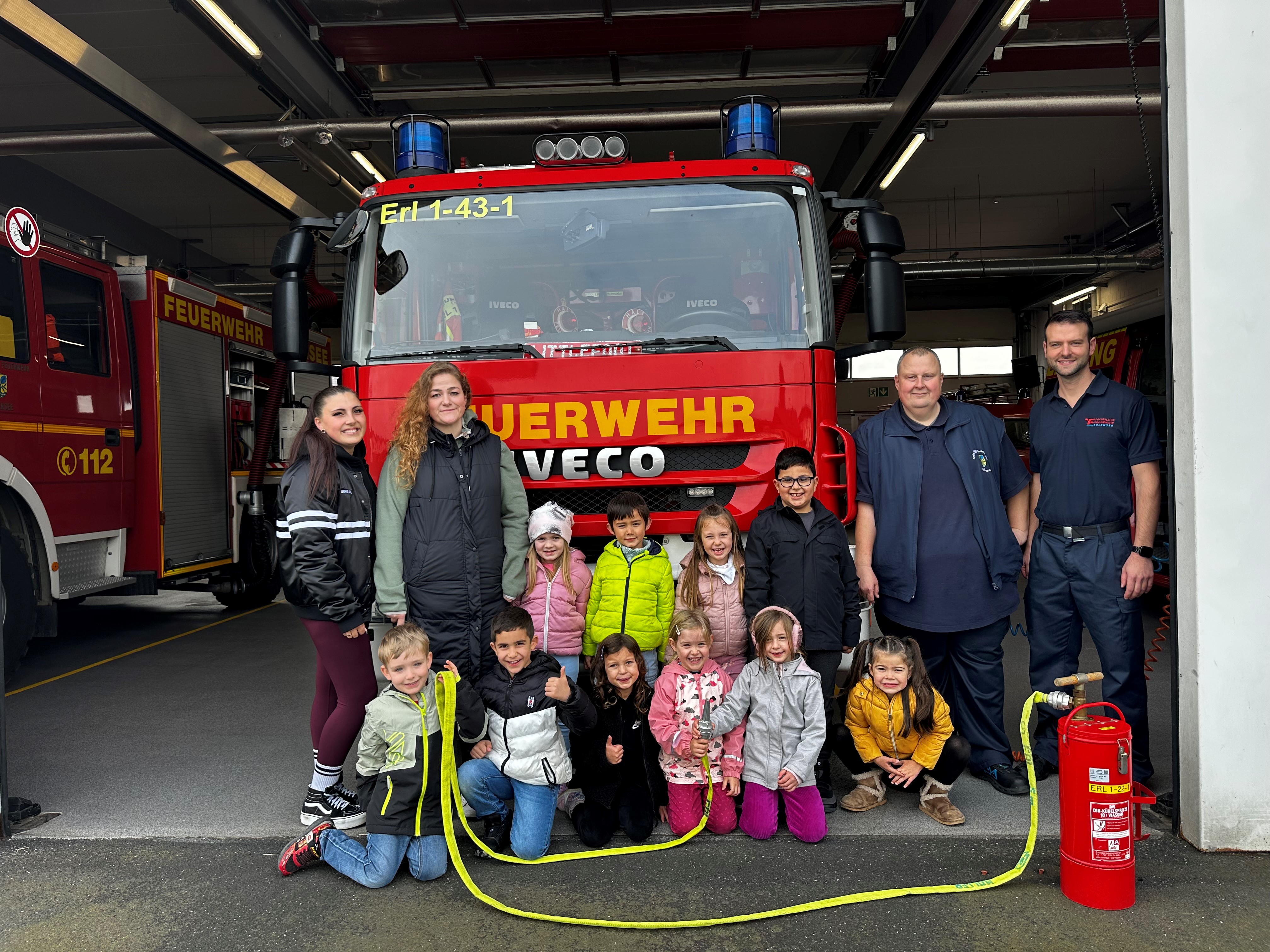 Kinder mit Erzieherinnen und Feuerwehrmänner vor einem großen Feuerwehrauto