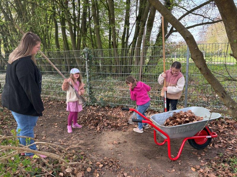 Drei Kinder rechen Laub zusammen