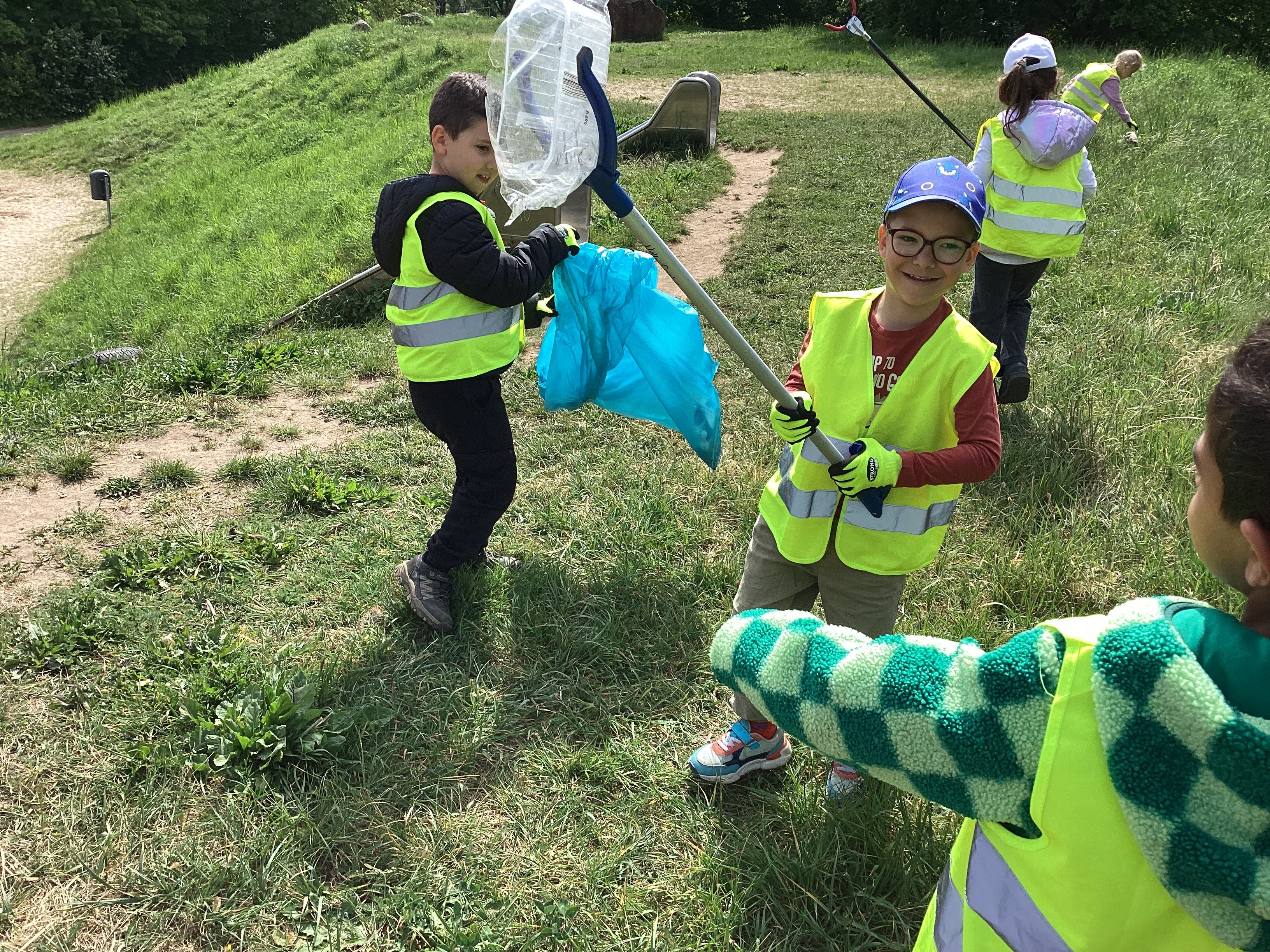 Kinder sammeln mit Greifern Müll auf dem Spielplatz