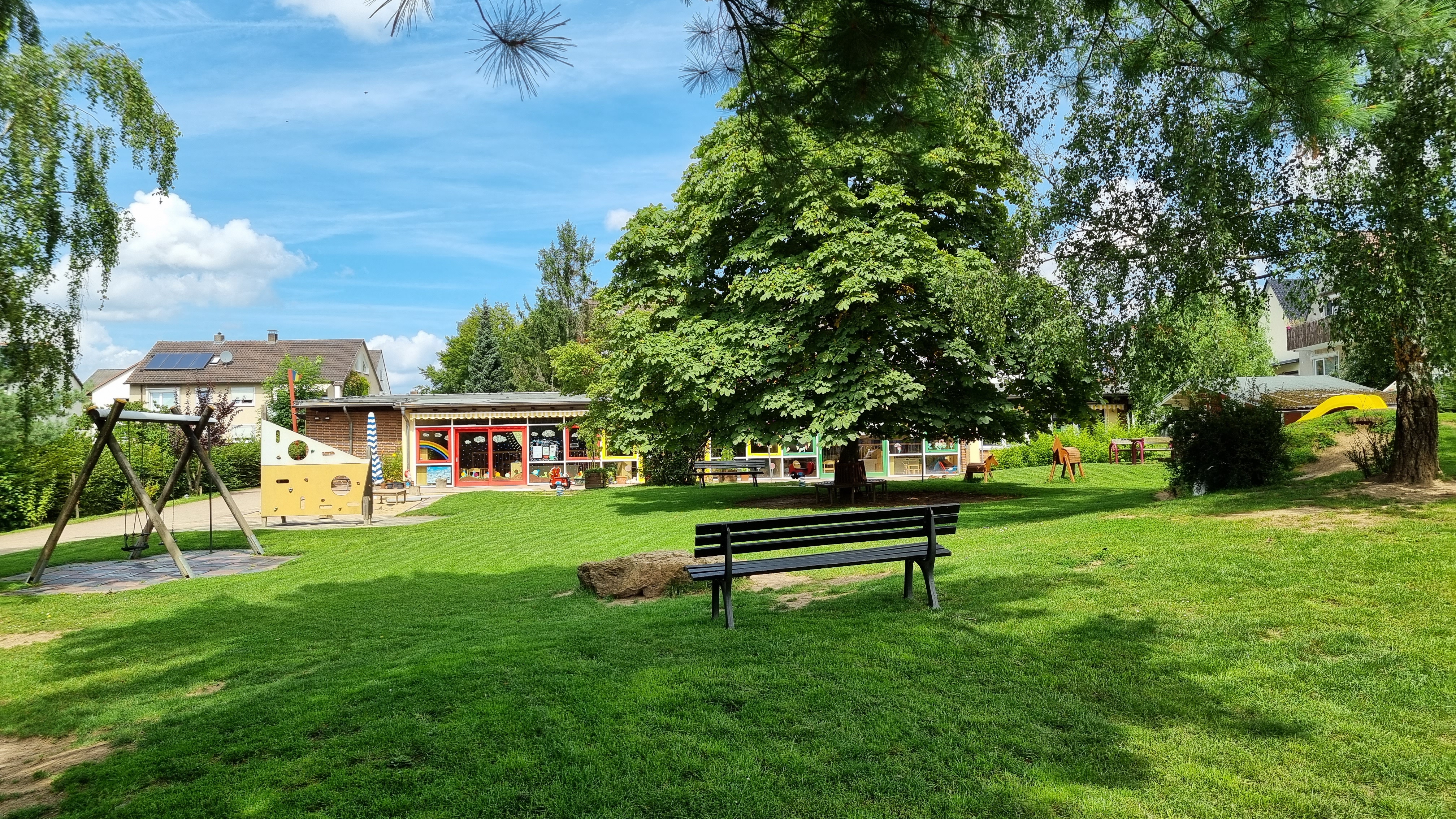 Der Gartenbereich des Kigas Am Park mit Rutsche, Bäumen und Spielgeräten.