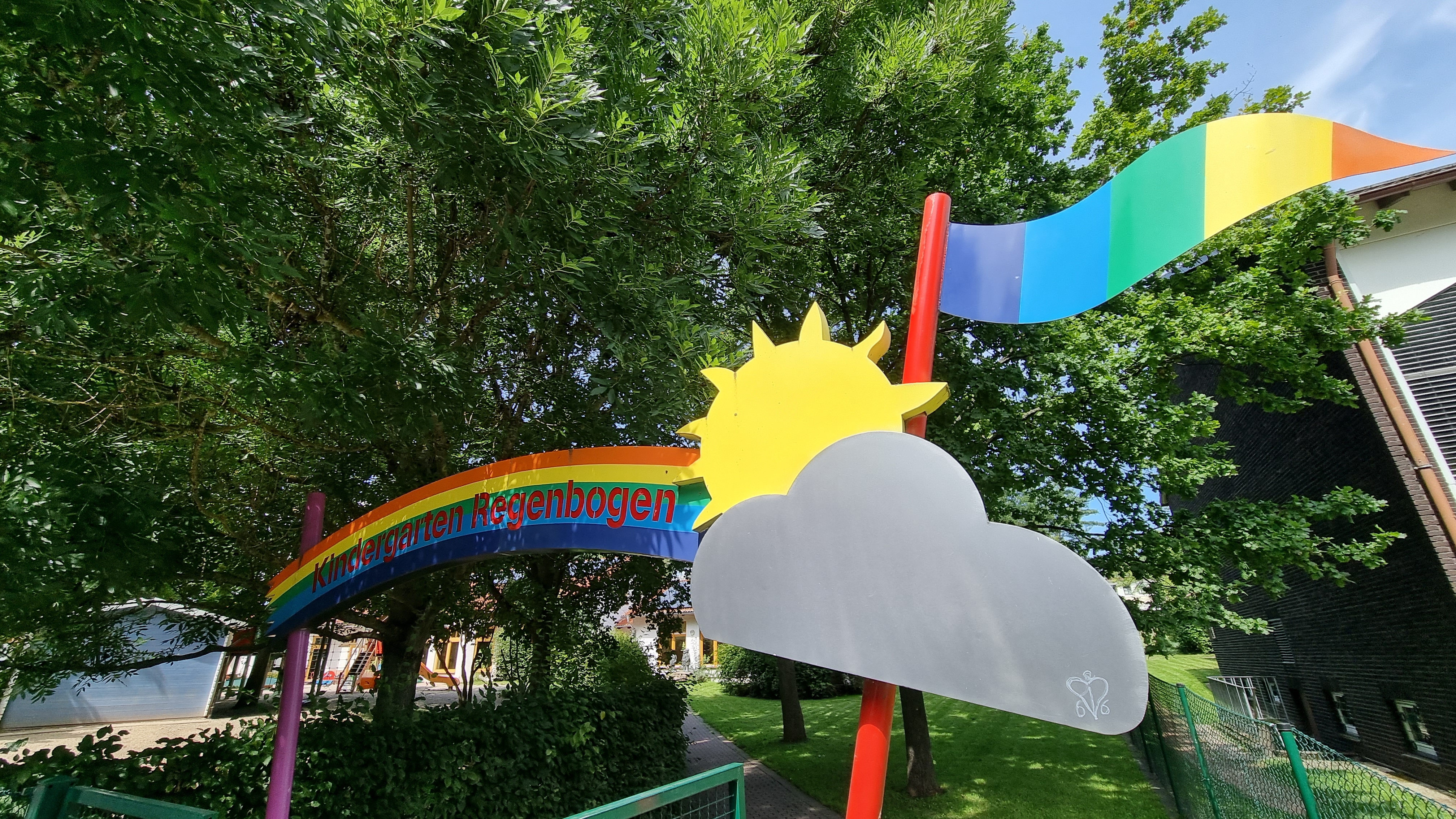 Das Begrüßungsportal des Kigas Regenbogen mit Sonne, Wolke, wehender Fahne und dem namensgebenden Regenbogen.